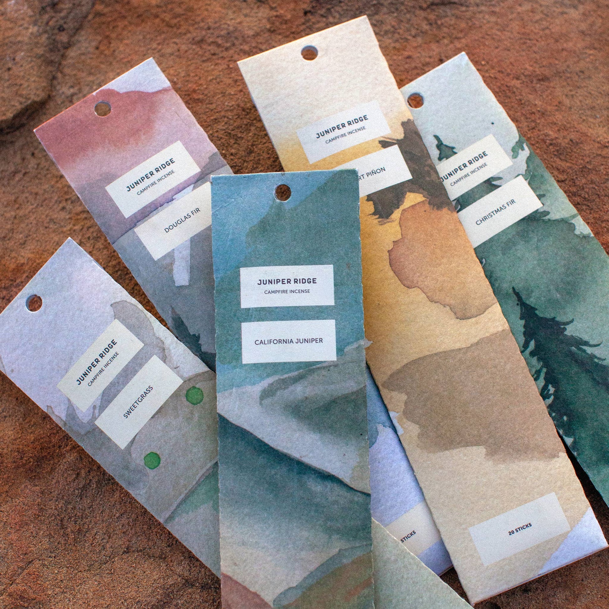 Set of Juniper Ridge Campfire Incense in a variety of scents and colors on a wooden surface