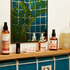Bathroom shelf with Juniper Ridge products including Desert Cedar Body Oil, Desert Cedar Essential Oil Desert Cedar Solid Perfume, Cologne, and Body Wash against a tiled blue wall