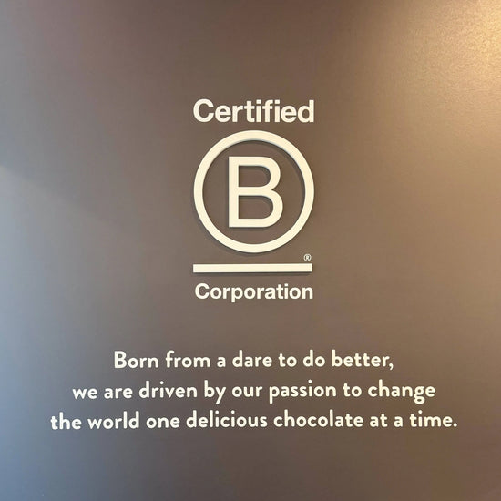 Certified B Corporation logo and text on a dark brown background, with the slogan 'Born from a dare to do better, we are driven by our passion to change the world one delicious chocolate at a time.'.