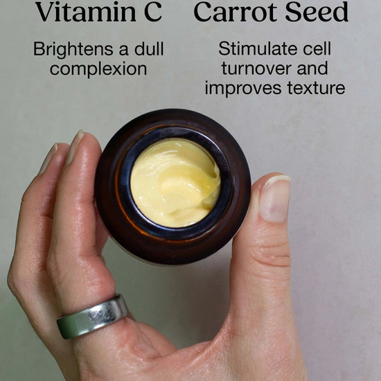 A hand holding a yellow cream by Simple Body called Beauty Balm calling out the benefits of Vitamin C which Brightens Dull Complexion and Carrot Seed Which Stimulates cell turnover and improves texture