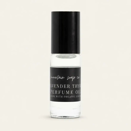 A clear glass bottle of Lavender Thyme Perfume Oil with a black cap and black label, showing the clear oil inside, set against a solid off-white background.