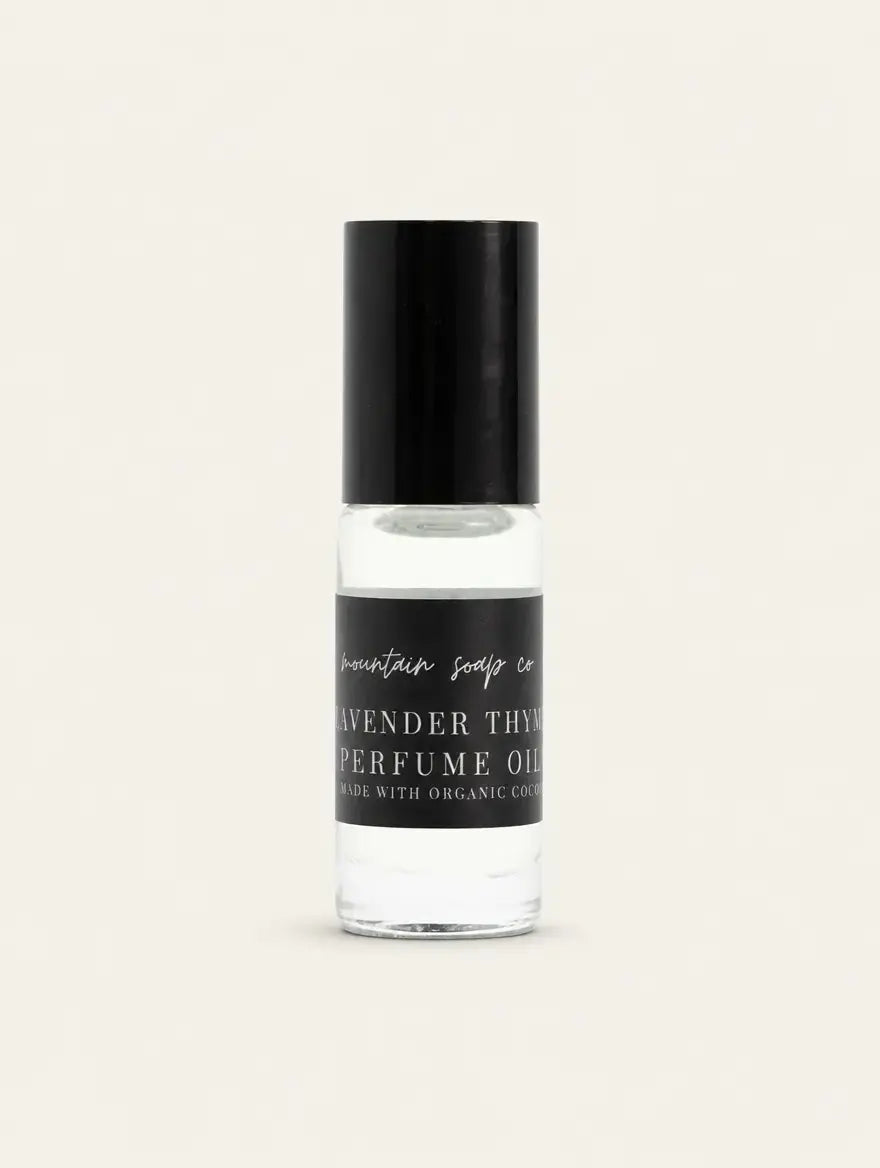 A clear glass bottle of Lavender Thyme Perfume Oil with a black cap and black label, showing the clear oil inside, set against a solid off-white background.