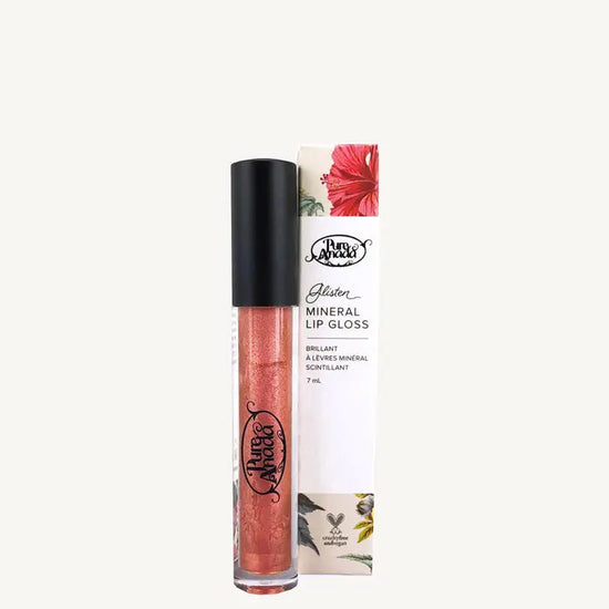 A photo of Pure Anada's Mineral Lip Gloss in Rose Gold with the tube standing up with a black lid and filled with a shimmery red - orange liquid on a tan background.