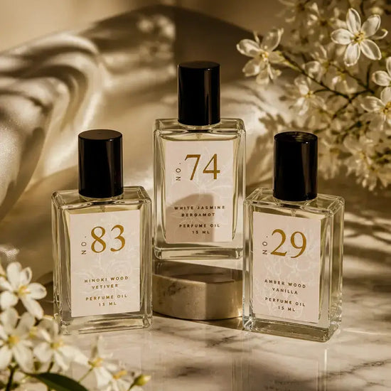 Three bottles of Luxe Perfume including No. 74, No. 83, and No. 29 with beige labels set around natural dried flowers on a marble countertop with shadows.