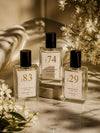 Three bottles of Luxe Perfume including No. 74, No. 83, and No. 29 with beige labels set around natural dried flowers on a marble countertop with shadows.