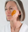 Woman with an swipe of Simple Body Pumpkin Enzyme Mask applied to her cheek against a plain background.