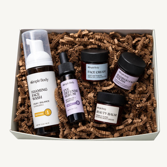 A Simple Body Mini Facial Kit that includes a Chamomile Foaming Face Wash Calm and Balance, Eye Defense Serum to Revitalize and Brighten, Face Cream for Moisture Renewal with Green Tea, Bamboo Face Polish Exfoliating Cleansing Scrub, and Beauty Balm Vitamin C Super Boosting Moisturizer with kraft shred on a white background