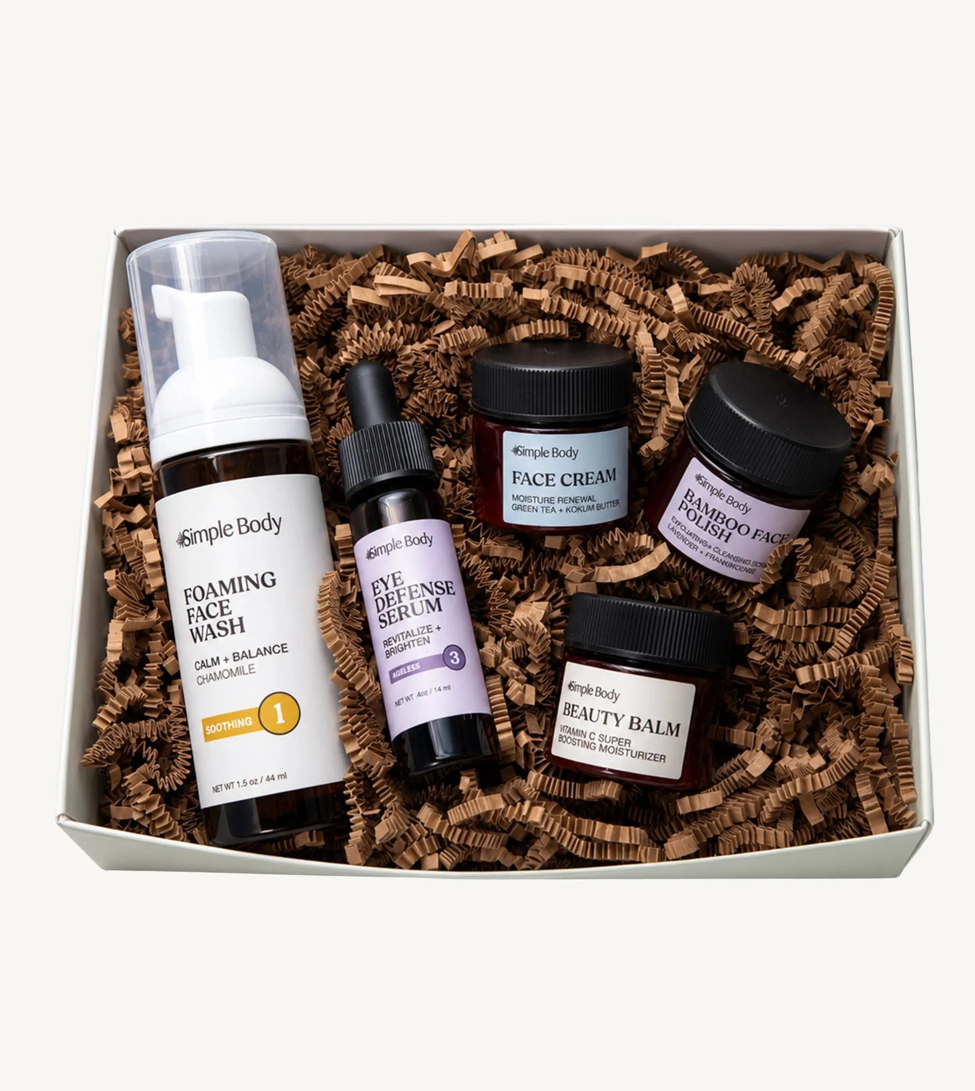 A Simple Body Mini Facial Kit that includes a Chamomile Foaming Face Wash Calm and Balance, Eye Defense Serum to Revitalize and Brighten, Face Cream for Moisture Renewal with Green Tea, Bamboo Face Polish Exfoliating Cleansing Scrub, and Beauty Balm Vitamin C Super Boosting Moisturizer with kraft shred on a white background