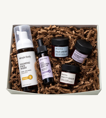 A Simple Body Mini Facial Kit that includes a Chamomile Foaming Face Wash Calm and Balance, Eye Defense Serum to Revitalize and Brighten, Face Cream for Moisture Renewal with Green Tea, Bamboo Face Polish Exfoliating Cleansing Scrub, and Beauty Balm Vitamin C Super Boosting Moisturizer with kraft shred on a white background
