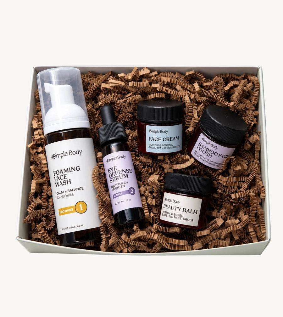 A Simple Body Mini Facial Kit that includes a Chamomile Foaming Face Wash Calm and Balance, Eye Defense Serum to Revitalize and Brighten, Face Cream for Moisture Renewal with Green Tea, Bamboo Face Polish Exfoliating Cleansing Scrub, and Beauty Balm Vitamin C Super Boosting Moisturizer with kraft shred on a white background
