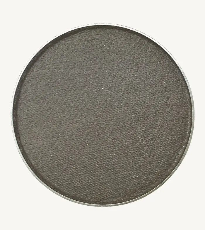 A photo of Pure Anada's Pressed Eye Color in Pewter which is a dark gray with a hint of shimmer on a tan background.