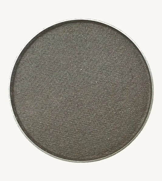 A photo of Pure Anada's Pressed Eye Color in Pewter which is a dark gray with a hint of shimmer on a tan background.