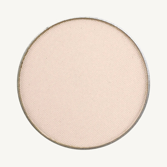 A photo of Pure Anada's Pressed Eye Color in Ivory Tower which is an off-white color with a pinkish hue on a tan background.
