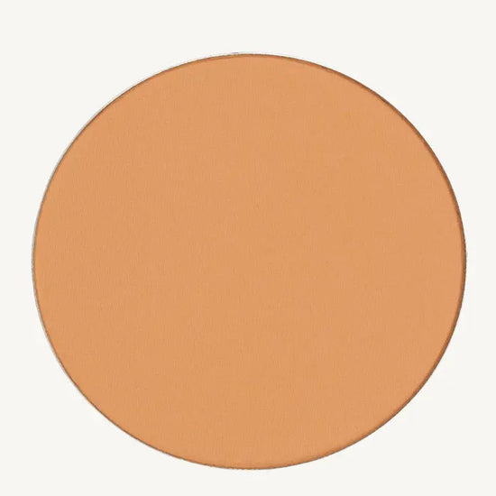 A photo of Pure Anada's Pressed Foundation Powder in Medium which is a warm peach honey color on a tan background.