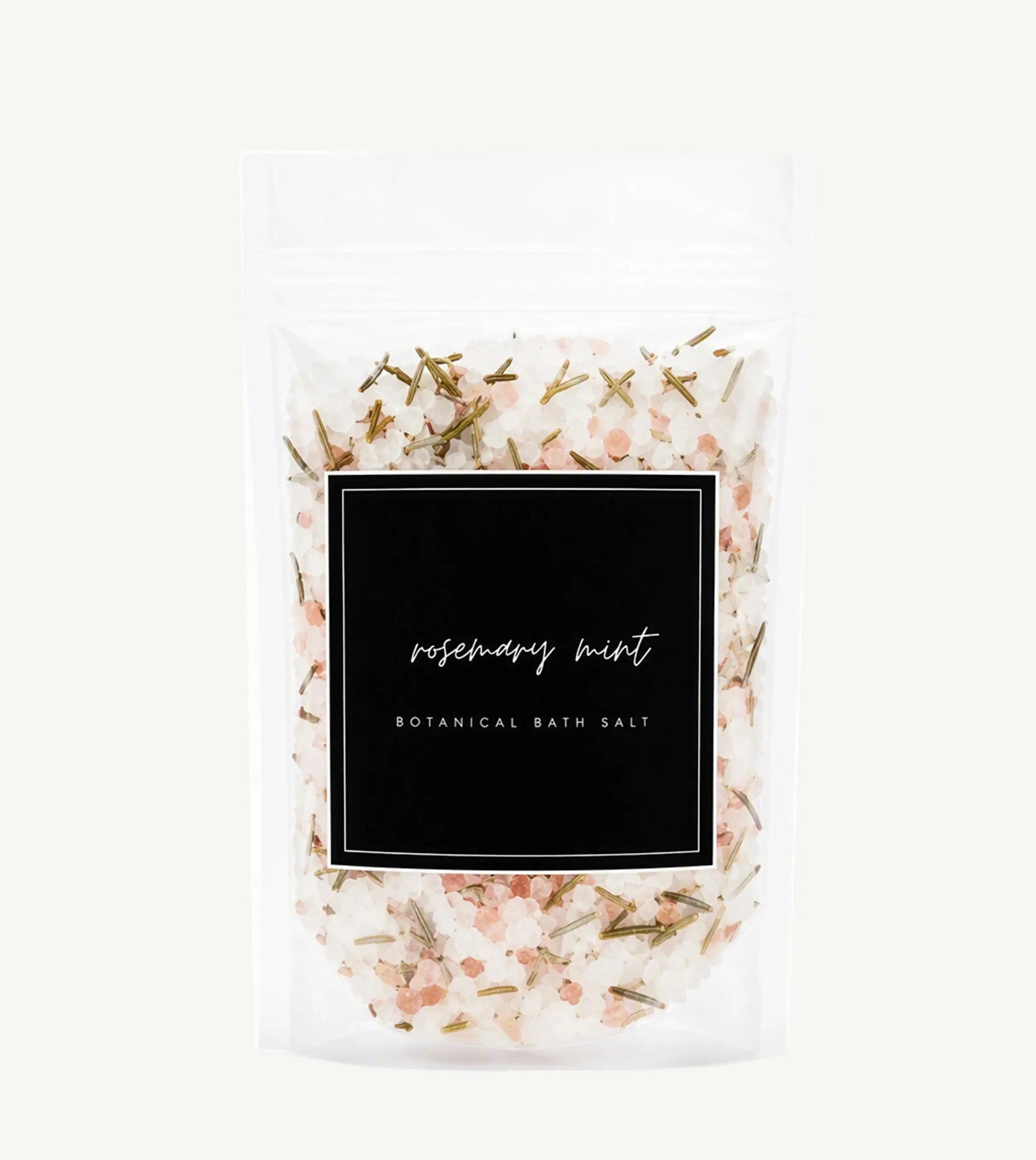 A clear stand-up pouch of rosemary mint botanical bath salt, showing the white bath salts mixed with pink crystals and green herbs through a black label on a light gray background.