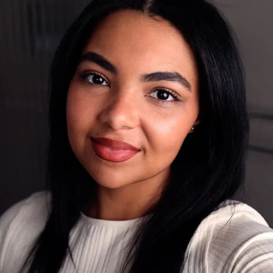 Woman with long dark hair wearing a light gray sweater against a neutral background with a warm orange brown lip color.