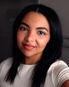 Woman with long dark hair wearing a light gray sweater against a neutral background with a warm orange brown lip color.