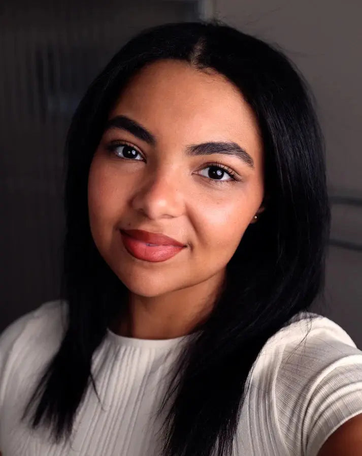 Woman with long dark hair wearing a light gray sweater against a neutral background with a warm orange brown lip color.