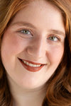 Close-up of a person with red hair and green eyes, wearing orange-brown warm lipstick by Pure Anada.
