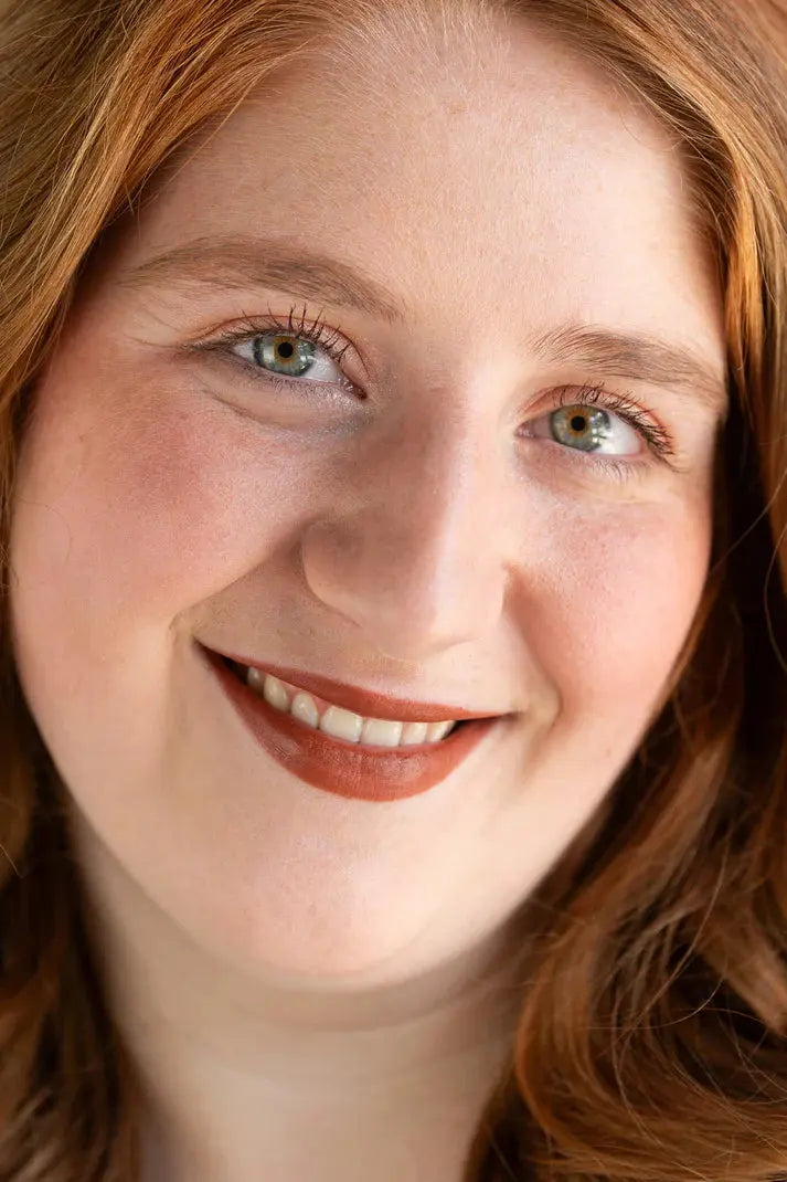 Close-up of a person with red hair and green eyes, wearing orange-brown warm lipstick by Pure Anada.