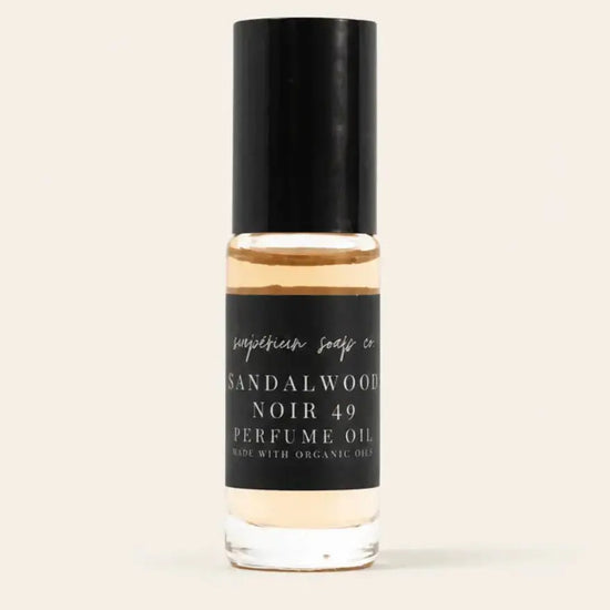 A bottle of Sandalwood Noir 49 Perfume Oil by Benjamin Soap Co, featuring a black cap and a black label with white text, set against a solid light beige background.