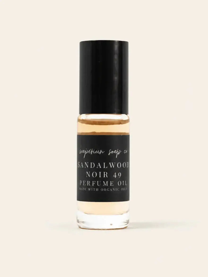 A bottle of Sandalwood Noir 49 Perfume Oil by Benjamin Soap Co, featuring a black cap and a black label with white text, set against a solid light beige background.