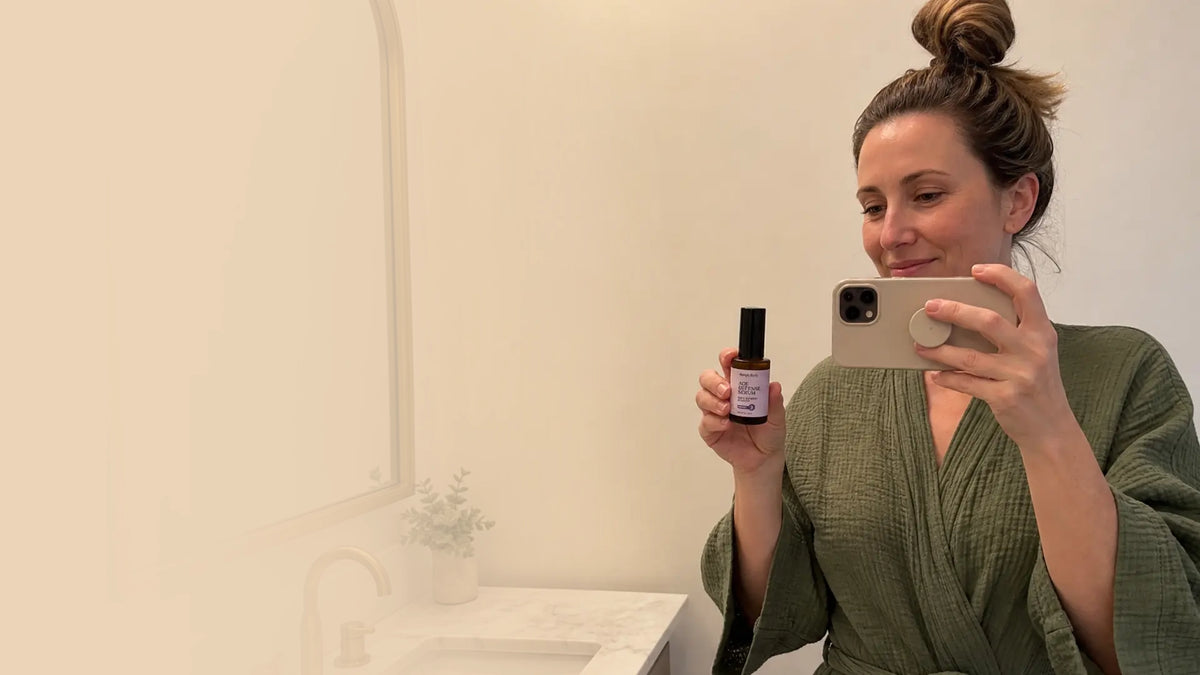 A Woman takes a selfie in a bathroom with Simple Body Age Defense Serum. AI