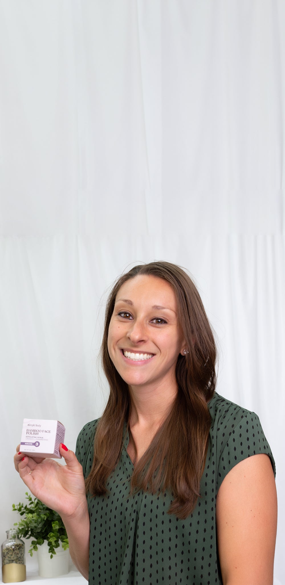 Smiling woman holding Simple Body Bamboo Face Polish skincare product against a bright white background