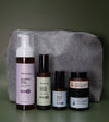 A Starter Skincare Kit for acne-prone skin with a foaming face wash, Clean Sweep Toner, Nightly Face Serum, Beauty Balm, Face Cream, and a gray cosmetic bag on a green background.