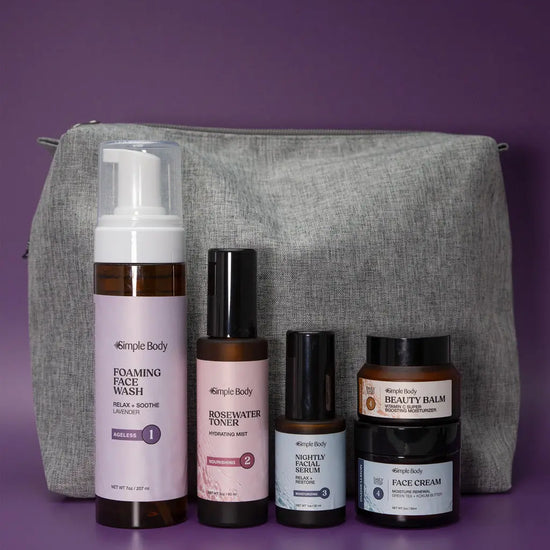 A Starter Skincare Kit for mature skin with a foaming face wash, Rosewater Toner, Nightly Face Serum, Beauty Balm, Face Cream, and a gray cosmetic bag on a purple background.
