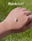 Hand holding a small white stone against a grassy background with 'thinksun' branding.