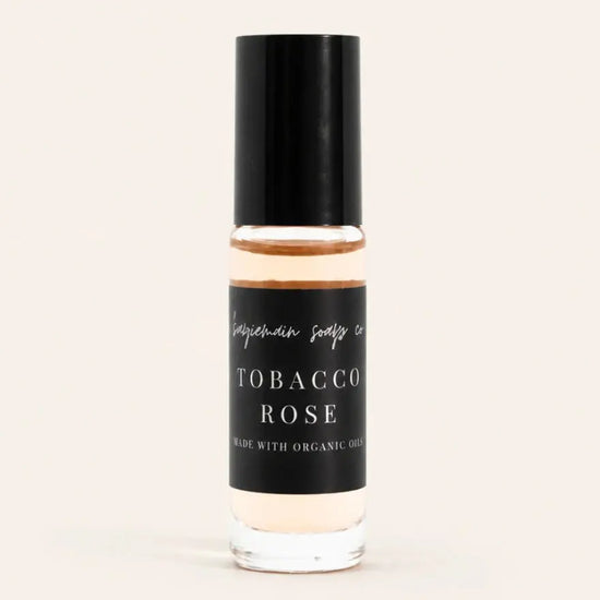 A small glass bottle of Robacco Rose Perfume Oil from Benjamin Soap Co with a black cap and black label, containing a warm amber liquid, centered on a light cream background.