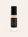 A small glass bottle of Robacco Rose Perfume Oil from Benjamin Soap Co with a black cap and black label, containing a warm amber liquid, centered on a light cream background.