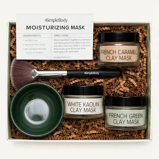 Simple Body Mask gift set in a white box filled with brown crinkle paper. The set includes three jars of clay masks (French Caramel Clay Mask, White Kaolin Clay Mask, and French Green Clay Mask), a dark green bowl, a makeup brush, and an instruction card.