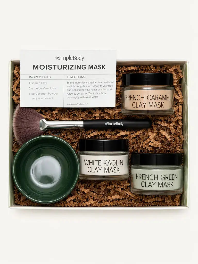 Simple Body Mask gift set in a white box filled with brown crinkle paper. The set includes three jars of clay masks (French Caramel Clay Mask, White Kaolin Clay Mask, and French Green Clay Mask), a dark green bowl, a makeup brush, and an instruction card.