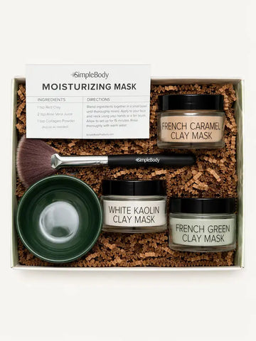 Simple Body Mask gift set in a white box filled with brown crinkle paper. The set includes three jars of clay masks (French Caramel Clay Mask, White Kaolin Clay Mask, and French Green Clay Mask), a dark green bowl, a makeup brush, and an instruction card.