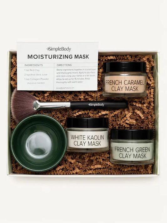 Simple Body Mask gift set in a white box filled with brown crinkle paper. The set includes three jars of clay masks (French Caramel Clay Mask, White Kaolin Clay Mask, and French Green Clay Mask), a dark green bowl, a makeup brush, and an instruction card.