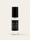 A small clear glass bottle of Vetiver 57 perfume oil with a black cap and a black label, centered on a warm off-white background.