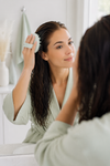 An image of a woman using a mint green hair and scalp brush on wet hair. Image generated via AI.