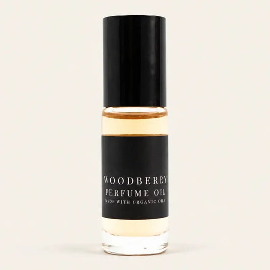A small glass bottle of Woodberry Perfume Oil from Benjamin Soap Co with a black cap and black label, containing a warm amber liquid, centered on a light cream background.