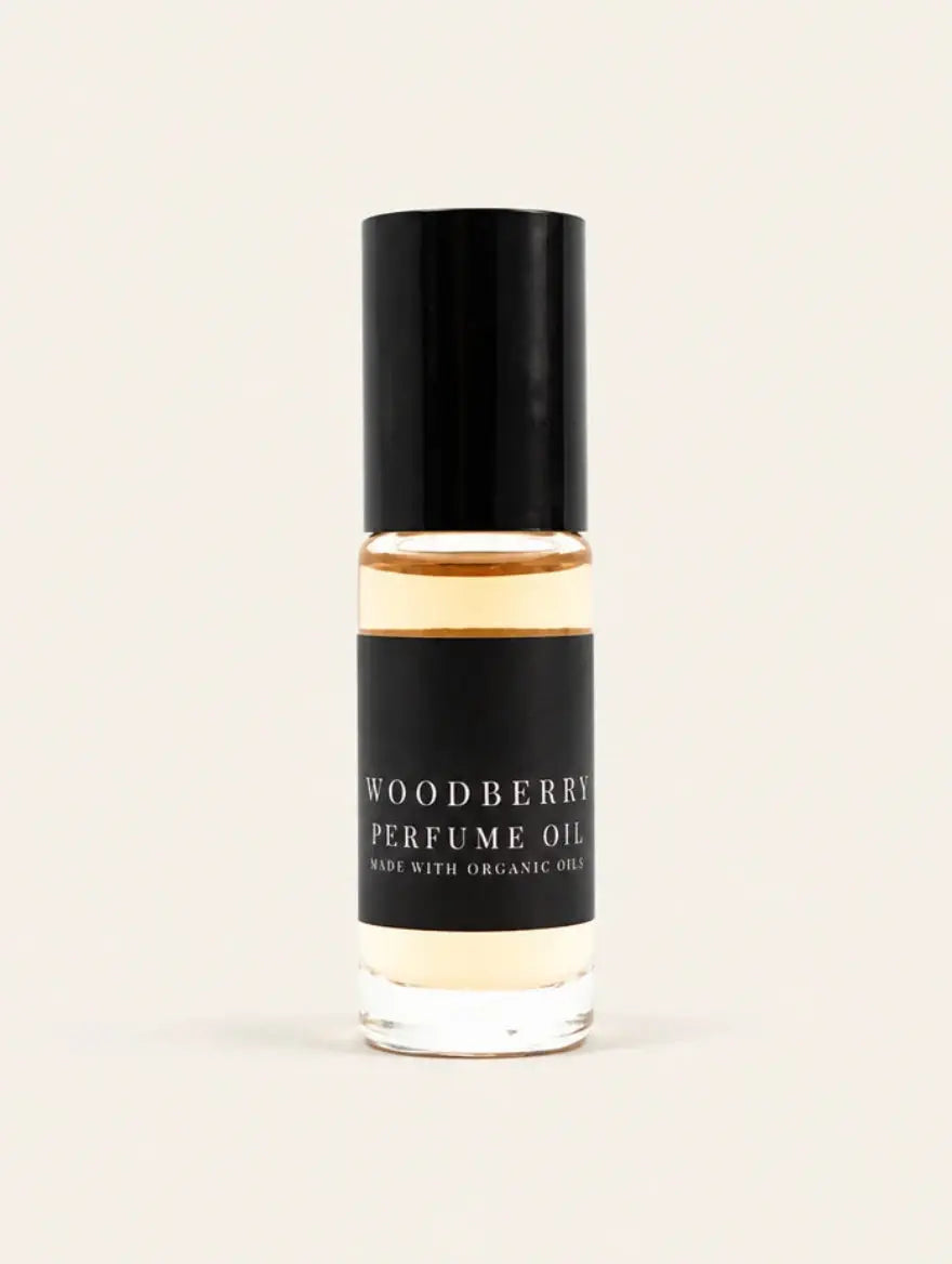 A small glass bottle of Woodberry Perfume Oil from Benjamin Soap Co with a black cap and black label, containing a warm amber liquid, centered on a light cream background.