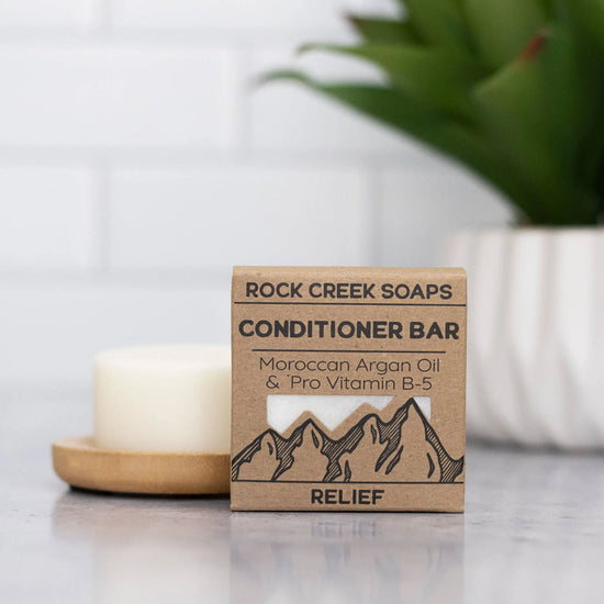 Rock Creek Soaps conditioner bar packaging on a surface with a candle and plant in the background