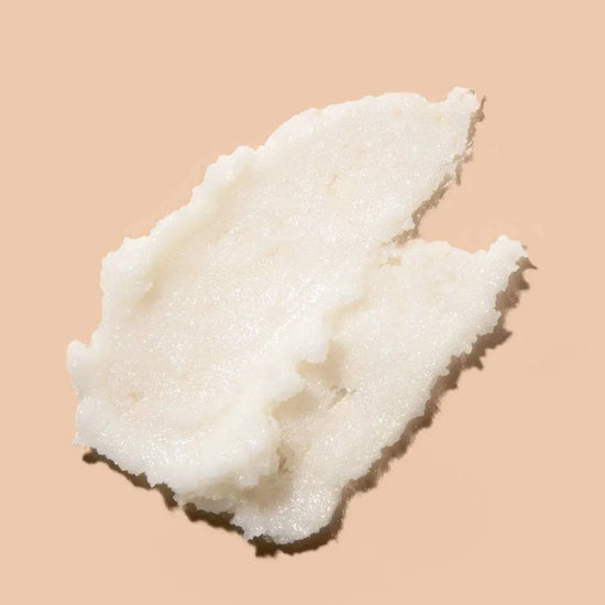 A dollop of white creamy body scrub photographed on a solid peach-beige background.