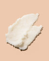 A dollop of white creamy body scrub photographed on a solid peach-beige background.