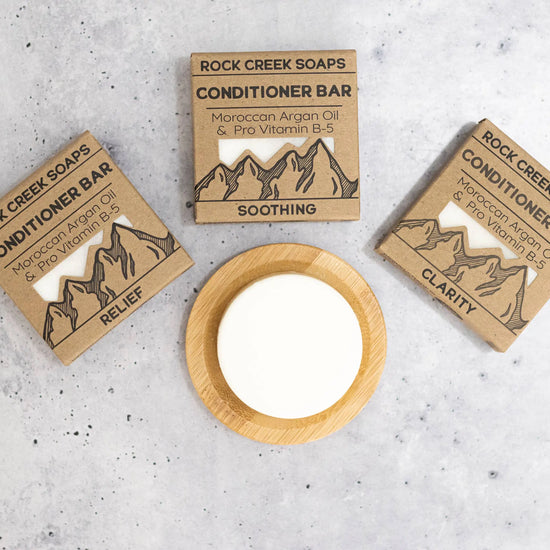 Three Rock Creek Soaps conditioner bars with packaging on a gray surface