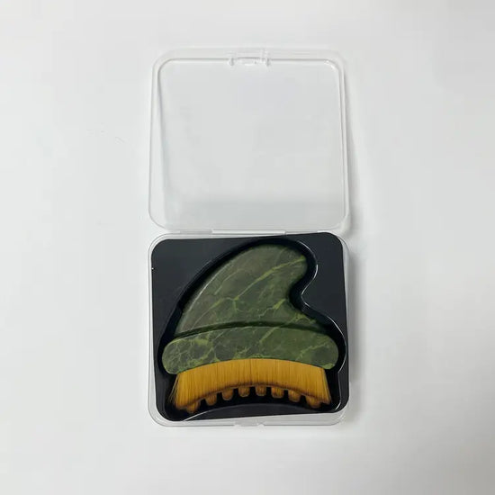 A green marbled lymphatic massage tool with a yellow bristle brush resting on a black insert inside a clear plastic case, shown on a plain white background.