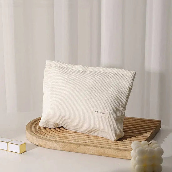 Beige corduroy cosmetic bag on a wooden stand with a minimal background