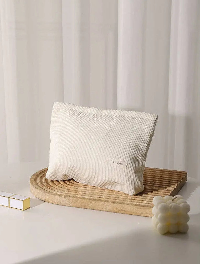 Beige corduroy cosmetic bag on a wooden stand with a minimal background