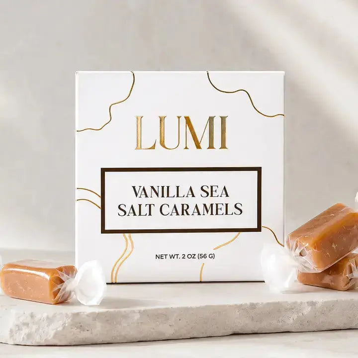 LUMI Vanilla Sea Salt Caramels in a white box with gold accents, styled on a light stone surface with unwrapped caramel bars on each side.
