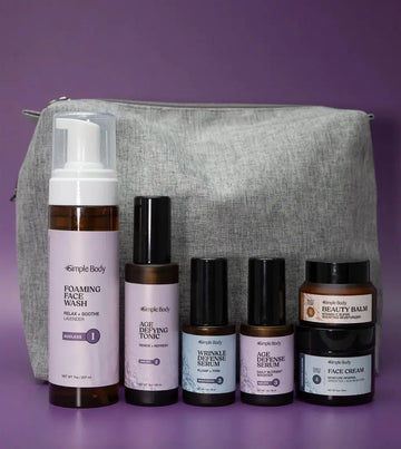 An Age Supporting Skincare Kit including a Foaming Face Wash, Age Defying Tonic, Wrinkle Defense Serum, Age Defense Serum, Beauty Balm, and Face Cream with a gray cosmetic bag on a purple background+